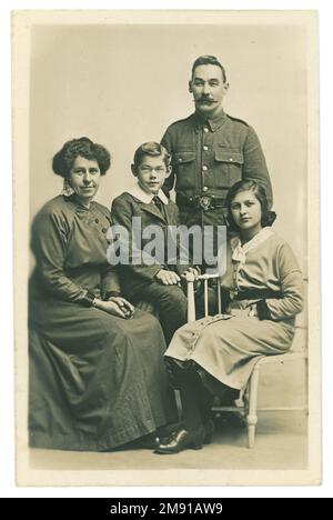 Original WW1 era studio portrait postcard family group posing for a photograph together. The children sit with their mother and father. The girl is of teenage years. All our in their Sunday best clothes. The father is in uniform and is possibly a Royal Marines Light Infantryman as indicated from his belt buckle design. Perhaps the soldier is on leave or about to go to the front. Dated Christmas 1915 on the reverse of the card, U.K. Stock Photo