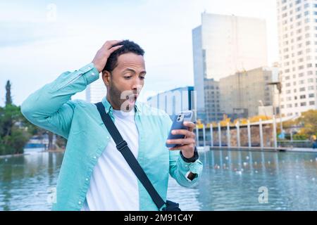 Young black man in the street looking at the phone with a surprised expression. Stock Photo
