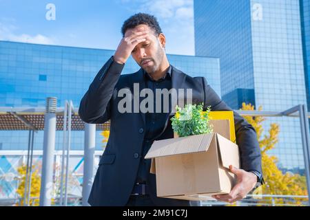 African American businessman fired with cardboard box with office supplies standing sad outdoors. Stock Photo