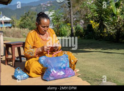 Dolakha District, Nepal - December 2022 -  Senior Woman at home  in the backyard knotting  wool ornament Stock Photo