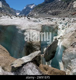 The glacial stream on the glacier Mer de Glace with the Garand Jorasses in the background. Stock Photo