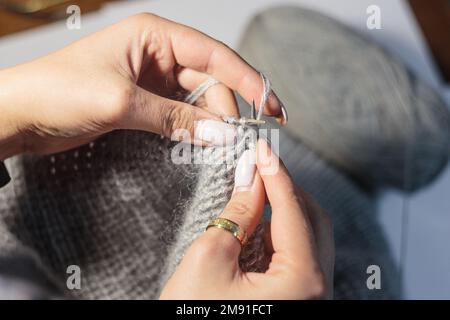 Close up hands knitting the dress from light blue wool on blurry background. Using circular needles Stock Photo