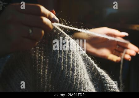 Close up hands knitting the dress from light blue wool on blurry background. Using circular needles Stock Photo