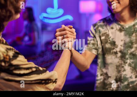 Greeting gesture of two happy young men in casual t-shirts enjoying party while standing in front of each other in apartment of their friends Stock Photo