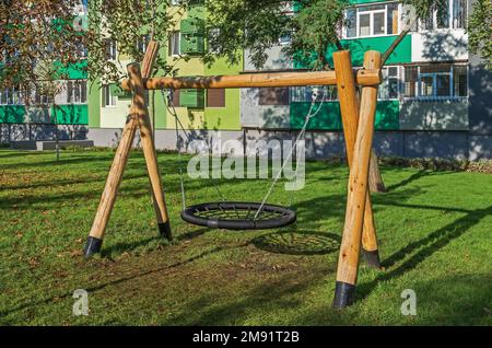 Swing for children birds nest made of logs, chains and ropes on the patio of multistorey building Stock Photo