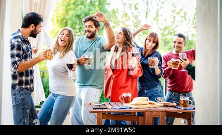 Young people having fun eating at home balcony dinner party - Happy friends drinking beer and wine at fancy alternative roof top venue together - Dinn Stock Photo