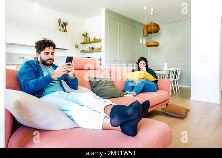 Bored couple in disinterest moment ignoring each other using mobile cell phone at home - Concept of apathy sadness with man and woman addicted Stock Photo