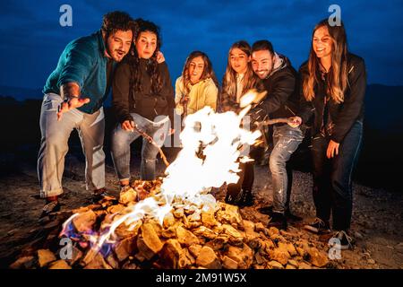 Young people having fun together at night party around bonfire - Wanderlust life style concept with happy friends traveler making themselves warm Stock Photo