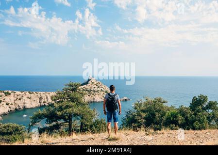 traveler the lone free man with backpack standing with his back to the sea on the beach during summer Stock Photo