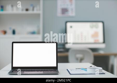 Laptop with blank white screen standing on workplace of modern veterinarian against computer monitor by wall with vet poster Stock Photo