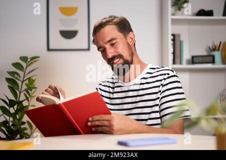 Caucasian young man sitting at home, concentrated reading a book.  Stock Photo