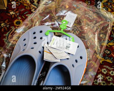 Paris, France - Dec 2, 2022: Living room carpet with pair of new Crocs sandals foam clogs in blue color with red inscription Stock Photo