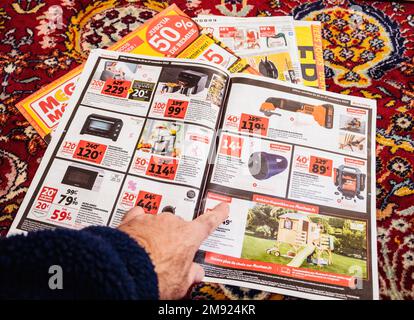 Paris, France - Dec 2, 2022: Man reading Auchan France leaflets supermarket chain selling furniture, electronics home object special black friday prices Stock Photo