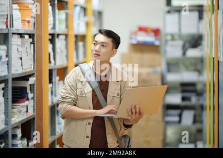 Portrait of college student with opened laptop searching for book for his research Stock Photo