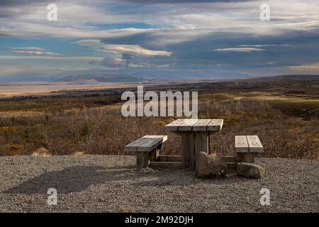 Country with trees, bushes, grass. Mountains on the horizon. Natural wooden desk and benches to sit, relax, eat and enjoy the panorama. Intense clouds Stock Photo