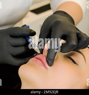 Young caucasian woman getting botox cosmetic injection in the lips. Beautiful woman gets botox injection in her face. Adult girl gets cosmetic injecti Stock Photo