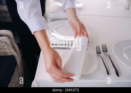 The waiter puts a white napkin on the plate. Beautiful table setting for a holiday without food. Stock Photo
