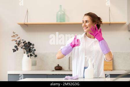 Attractive housewife holds a spray bottle with cleaning agent in her hand and shows a thumbs up.  Stock Photo