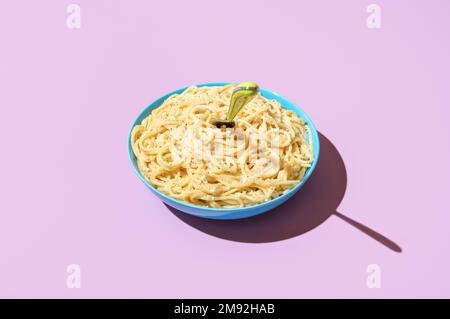 Bowl with spaghetti cacio e pepe minimalist on a vibrant colored table. Spaghetti with parmesan and black pepper on a purple background Stock Photo