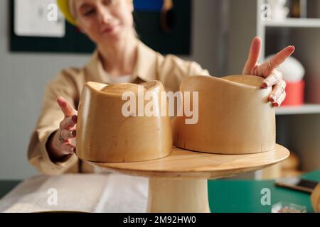 Selective focus on hands of creative woman touching wooden workpieces in form of hat upper part while working over new collection for sale Stock Photo