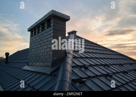 Chimney on house roof top covered with metallic shingles under construction. Tiled covering of building. Real estate development Stock Photo