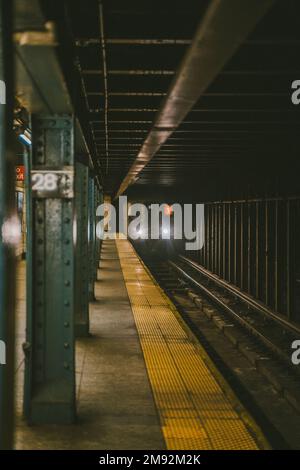 Old train with glowing headlights going through metal rails in empty metro at evening time Stock Photo