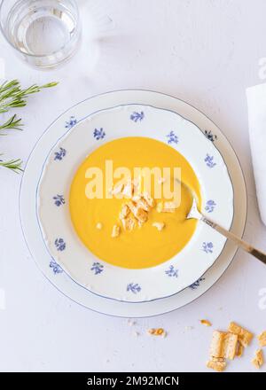 Top view of delicious pumpkin cream soup with crackers served in ceramic plate on white table near glass of water Stock Photo