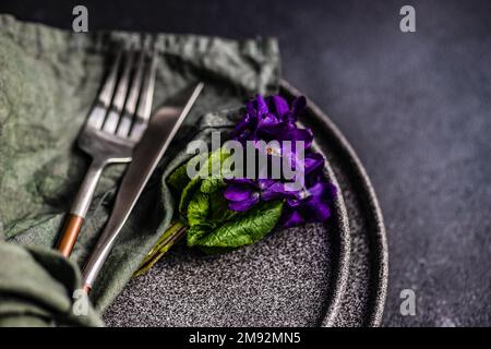 Spring table setting with wild blue viola flower on black plate set Stock Photo
