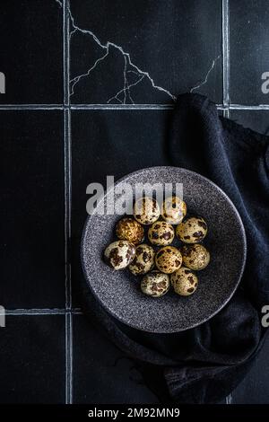 From above ceramic bowl with raw quail eggs on tiled table Stock Photo