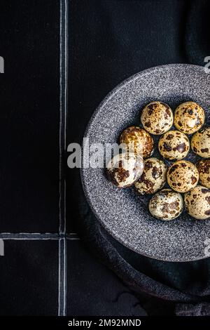 From above ceramic bowl with raw quail eggs on tiled table Stock Photo