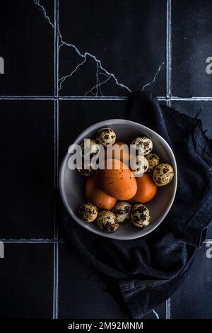 From above ceramic bowl with raw quail and chicken eggs on tiled table Stock Photo