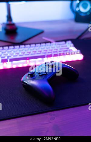 High angle of black wireless joystick placed near luminous computer keyboard on table Stock Photo