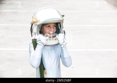 Isolated preteen child in silver space suit touching helmet and looking away while standing against white background Stock Photo