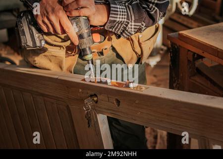 Anonymous male carpenter in casual clothes drilling metal detail while creating wooden door in workshop Stock Photo
