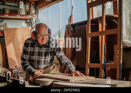 Mature male woodworker in glasses and casual clothes cutting