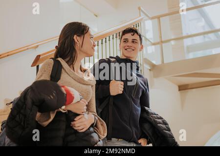 Low angle of positive friends in casual outfits with backpacks looking at each other while standing near staircase in university campus while talking Stock Photo