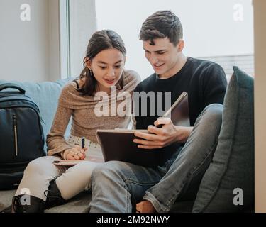 Smiling young students in casual clothes reading notes while preparing for exam together with cup of takeaway coffee in university library Stock Photo