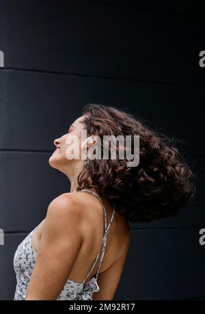 Charming young female with closed eyes smiling while listening to music in earphones against black background Stock Photo