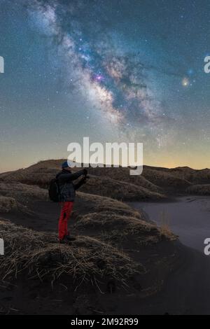 Remote view of male traveling photographer taking picture of night sky glowing stars of Milky Way in Lofoten Islands, Norway Stock Photo