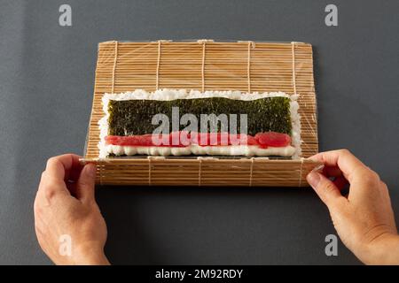 From above of crop anonymous person making sushi with rolling mat consisting of seaweed rice and salmon Stock Photo