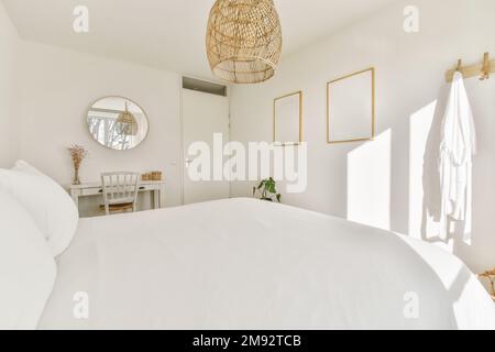 Modern bedroom with comfortable bed and soft pillows placed under lamp against mirror and blank photo frames hanging on wall Stock Photo
