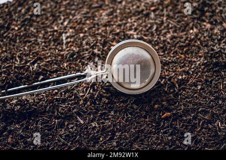 Top view of metal tea strainer placed on dried leaves of tea with fruits and flowers Stock Photo