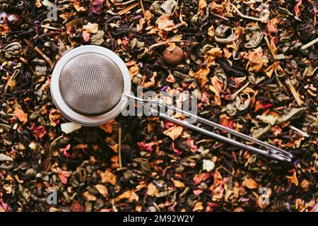 Top view of metal tea strainer placed on dried leaves of tea with fruits and flowers Stock Photo