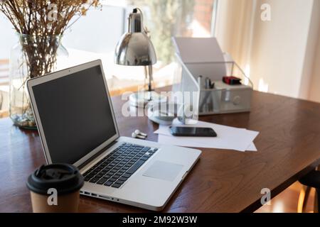 Interior of modern home workspace with wooden table and laptop and chair near big window in sunlit apartment Stock Photo