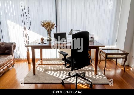 Interior of modern home workspace with wooden table and laptop and chair near big window in sunlit apartment Stock Photo