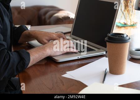 Cropped anonymous male freelancer sitting in armchair on table while using laptop and working on project in living room Stock Photo