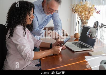 Concentrated multiracial coworkers discussing project while using tablet computer near laptop at wooden table in creative workspace Stock Photo