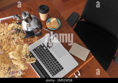 Top view of opened laptop and glasses placed on wooden table with cup of coffee and biscuits in home office Stock Photo