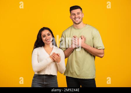 Smiling millennial arab guy and woman in casual clothes press their hands to chest, say thanks Stock Photo