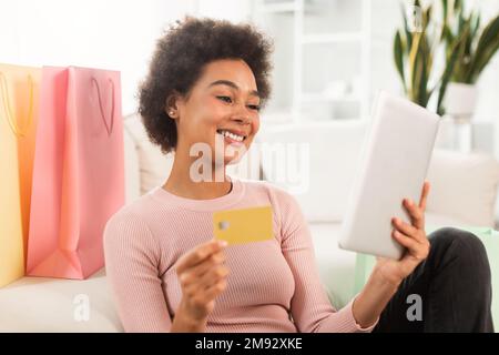 Smiling young mixed race female shopaholic with tablet, credit card checking financial account, use banking app Stock Photo